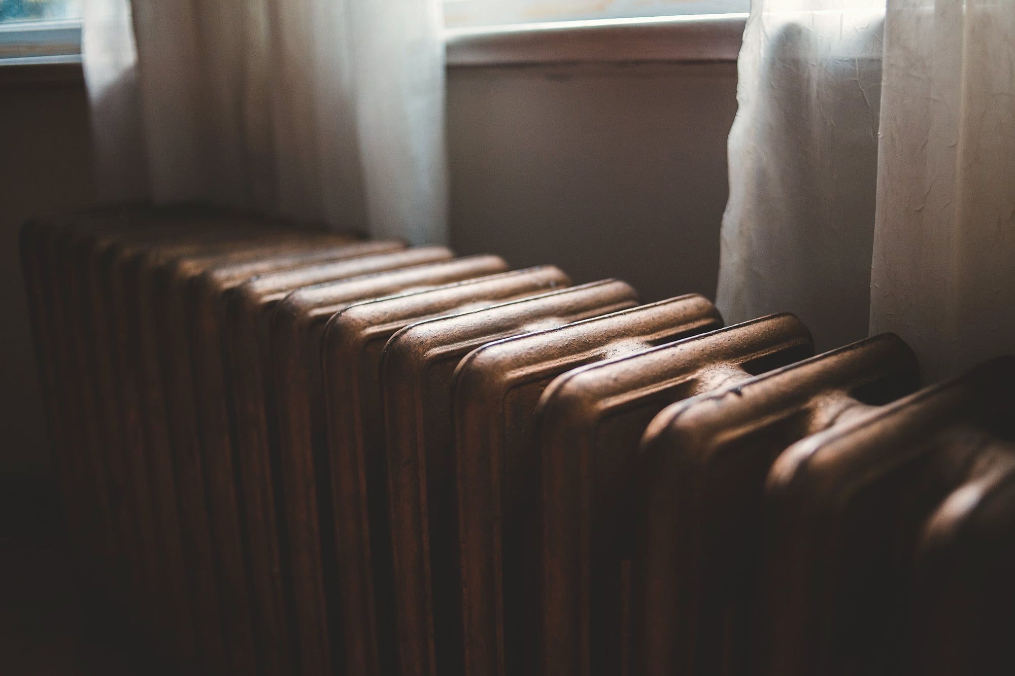 Un vieux radiateur en fonte sous une fenêtre voilée.