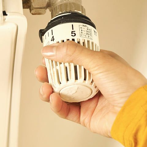 Une main règle un thermostat.